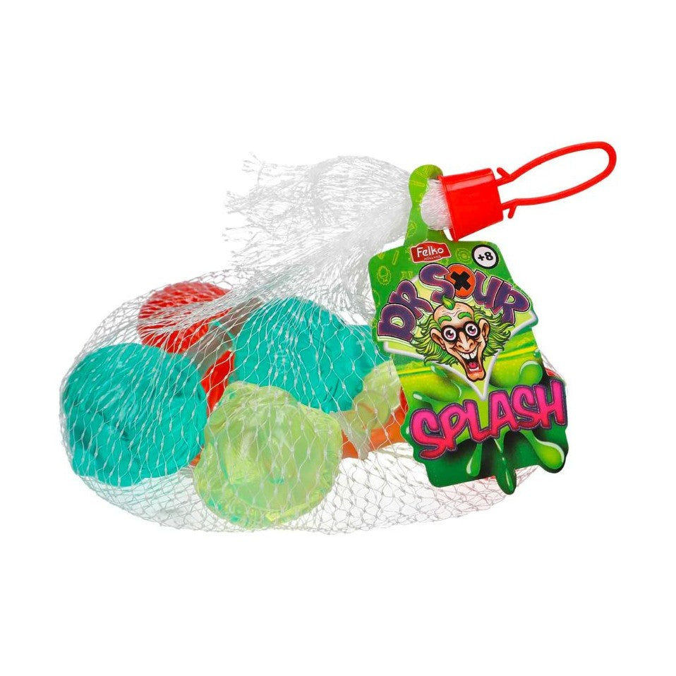 Un emballage en filet qui permet de voir des boules transparentes contenant des liquides de couleurs différentes ; jaune, rouge, bleu et une étiquette verte sur le côté droit avec un visage de Dr aux cheveux verts. Le tout sur fond blanc