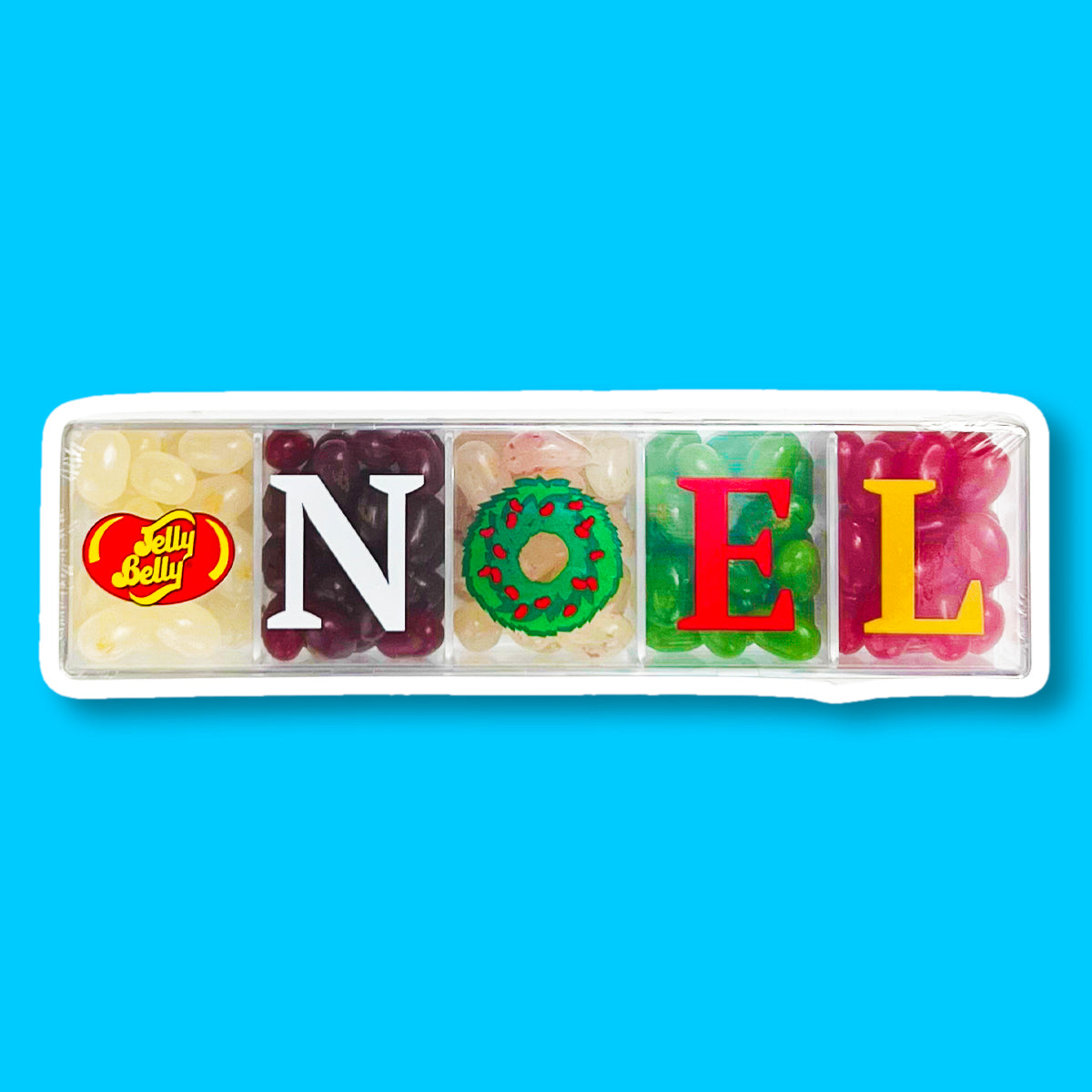 Une boite transparente avec 5 compartiments remplis de Jelly Belly jaune, blanc, rouge, verte et rose et une inscription « NOEL ». Le tout sur un fond bleu