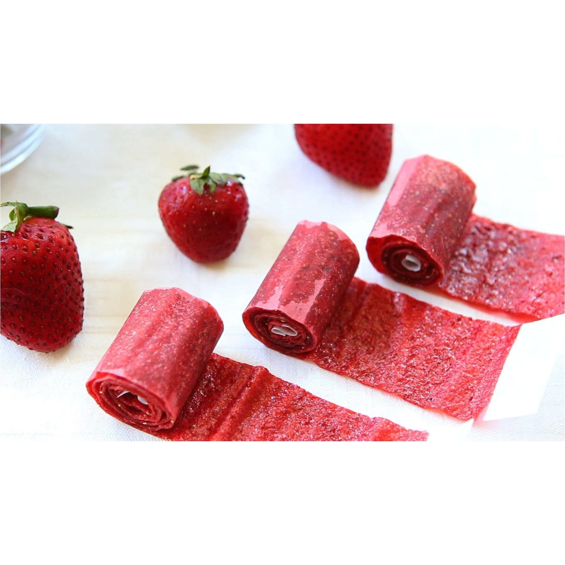 3 bonbons rouges enroulés devant 3 fraises sur une table avec une nappe blanche