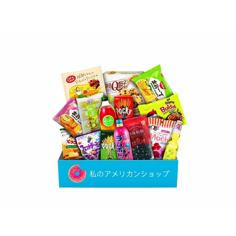 Un carton rectangulaire bleu contenant plein de snacks asiatiques comme des mochis/cookies, des biscuits en bâtonnet avec du chocolat vert des boules noirs de tapioca, une boisson jaune etc… Le tout sur fond blanc