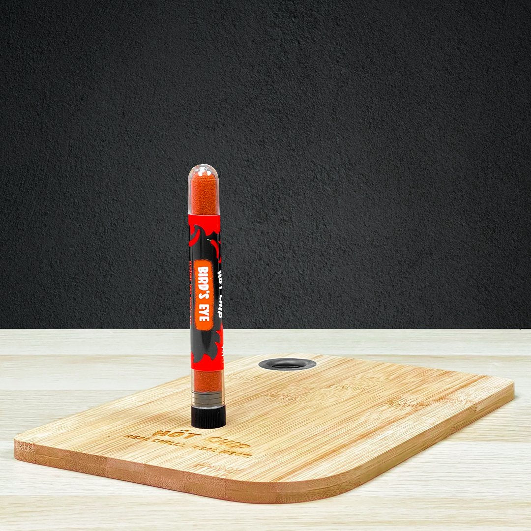 Une planche en bois sur une table en bois avec au-dessus une fiole en verre avec des épices rouges. Le tout devant un mur noir