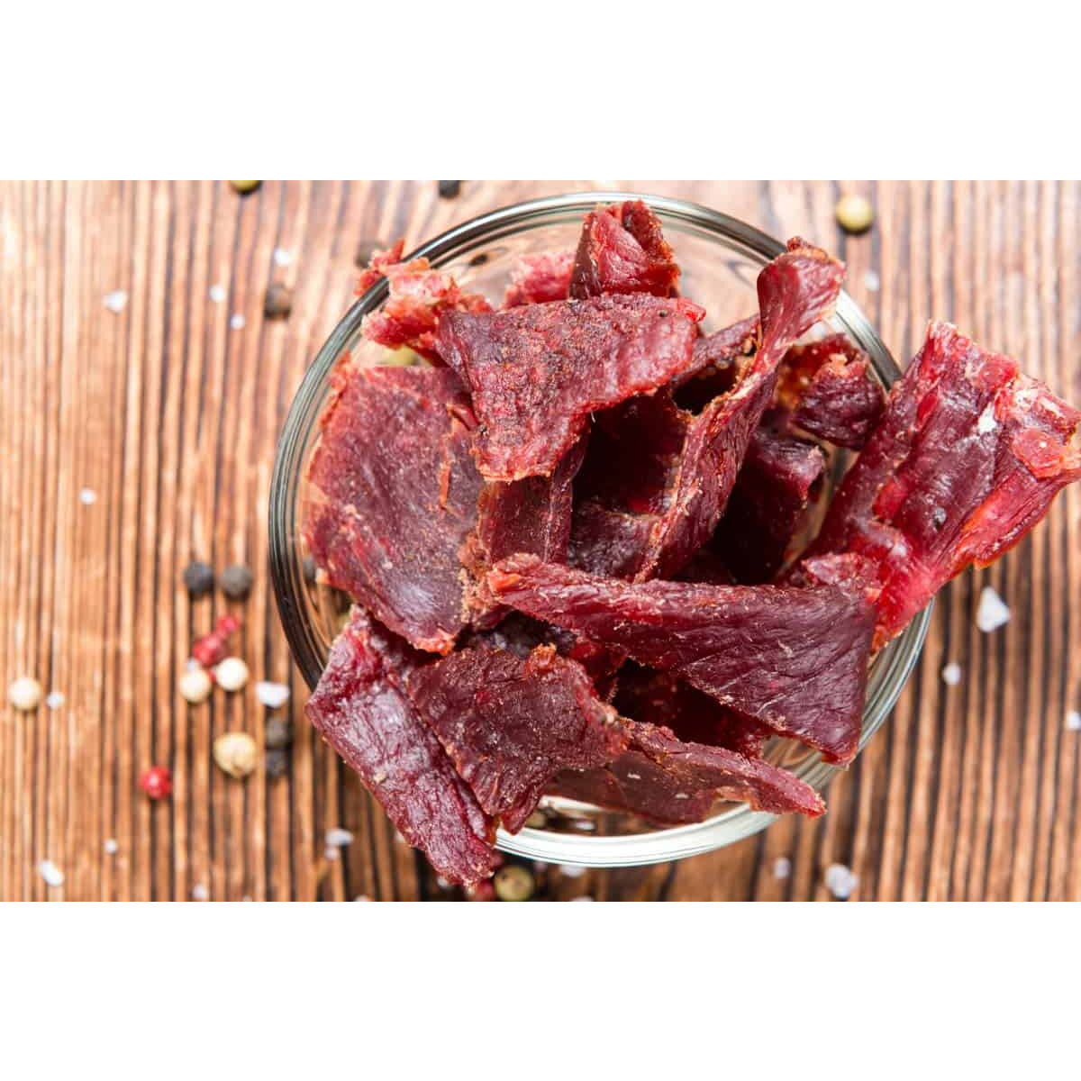 Un petit bol en verre avec des morceaux de viande séchée, sur une table en bois