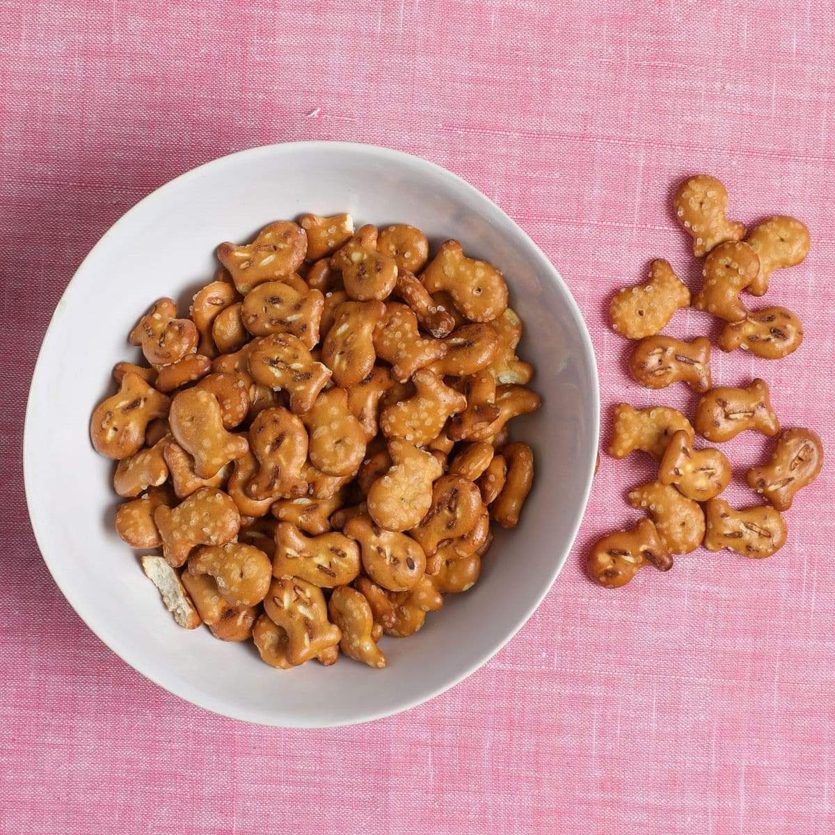 Un bol blanc avec des petits biscuits bruns en forme de poisson. Le tout sur une table avec nappes roses