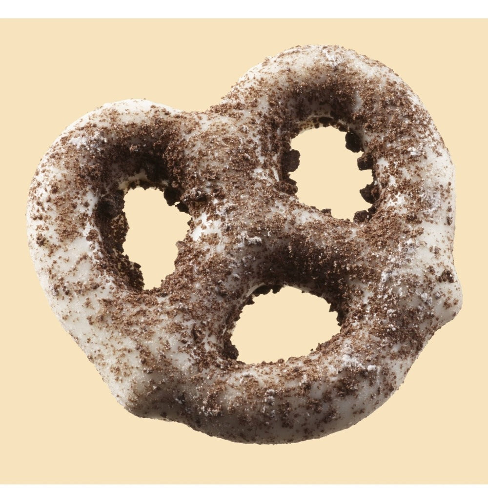 Un bretzel enrobé de chocolat blanc et saupoudrés poudre de cookies au chocolat sur un fond beige