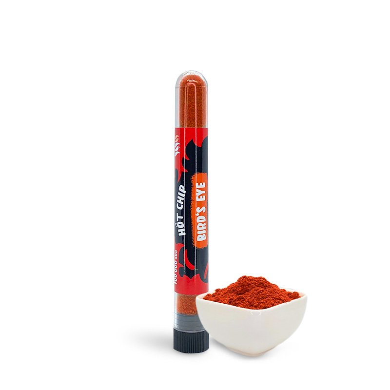 Une petite fiole transparente remplie d’une poudre rouge avec une étiquette rouge et noire, devant il y a un petit bol avec la même poudre rouge. Le tout sur fond blanc