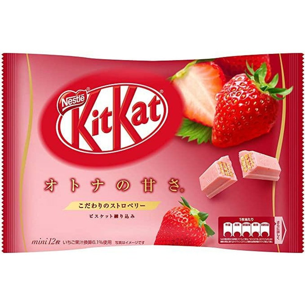 Un grand paquet rouge/rose avec en haut à droite 2 fraises et en bas un biscuit enrobé de chocolat rose. Le tout sur fond blanc