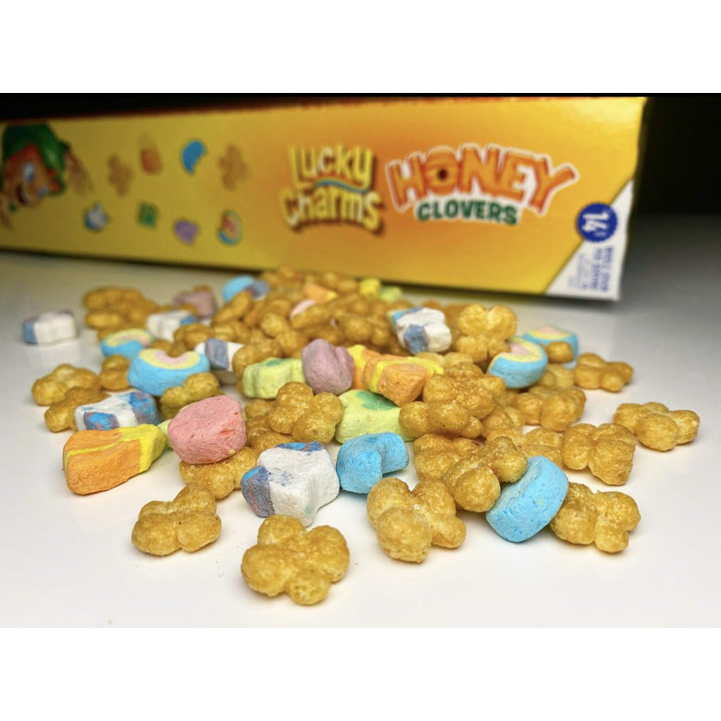 Un petit tas de céréales en forme de ronds, de trèfles et des petits petits marshmallows colorés sur une table blanche et derrière un emballage jaune 
