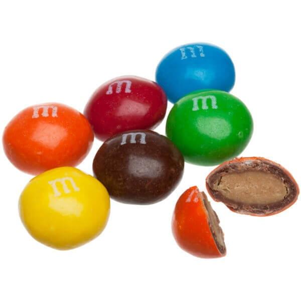 Plusieurs M&M’s bleu, rouge, orange, jaune, marron et vert. Et à droite une M&M’s orange coupé en 2, le tout sur fond blanc