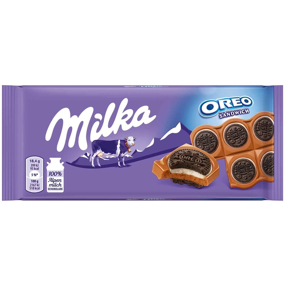 Un emballage mauve sur fond blanc avec inscrit à gauche « Milka » et en-dessous une vache blanche et mauve devant des montages. Sur le côté droit une tablette de Milka Oreo Sandwich avec un bout qui a été croqué 
