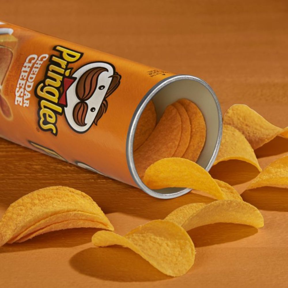 Un paquet en forme de cylindre orange ouvert, avec des chips jaunes qui sortent. Le tout sur une table jaune orangé