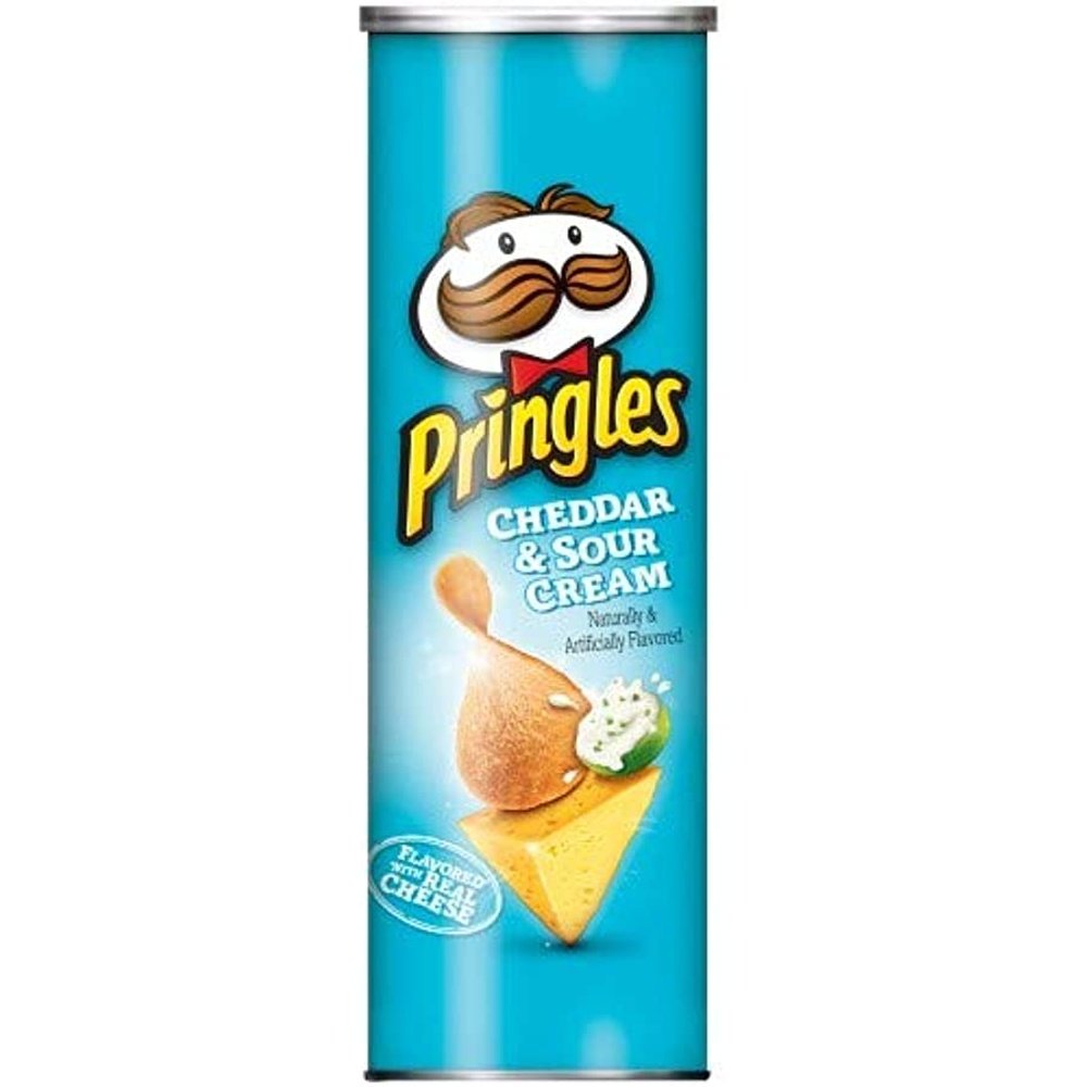 Un paquet en forme de cylindre bleu, au milieu il y a un morceau triangulaire de fromage avec une chips sur le dessus et à coté un bol vert rempli d’une sauce blanche